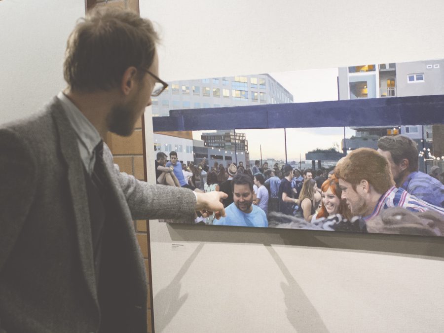 Painter and faculty member Nicholas Enevoldsen points to the detailed individuals in his photo-turned-portrait titled Opening Night.