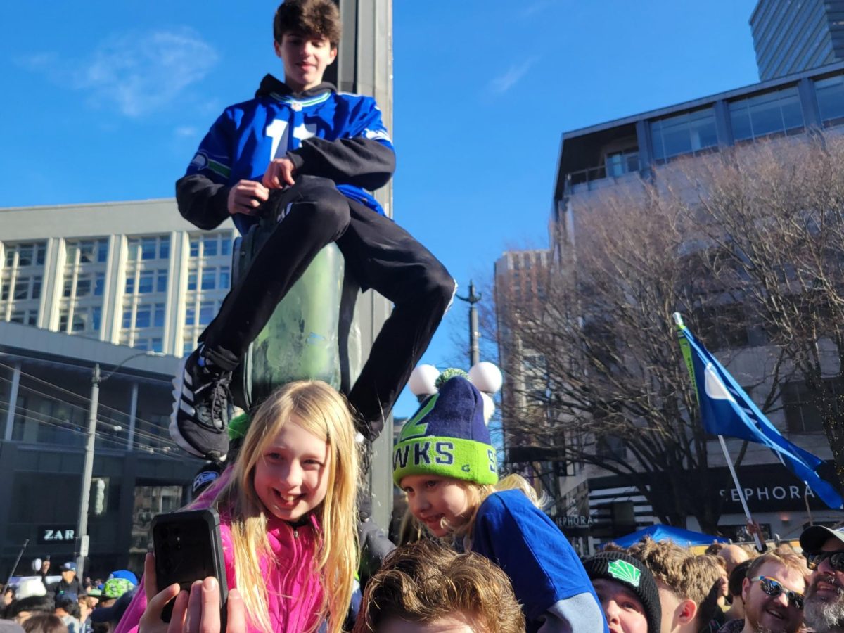 Seahawks fans climb walk signs or parent's shoulders to see the crowd and to, eventually, see the parade better.