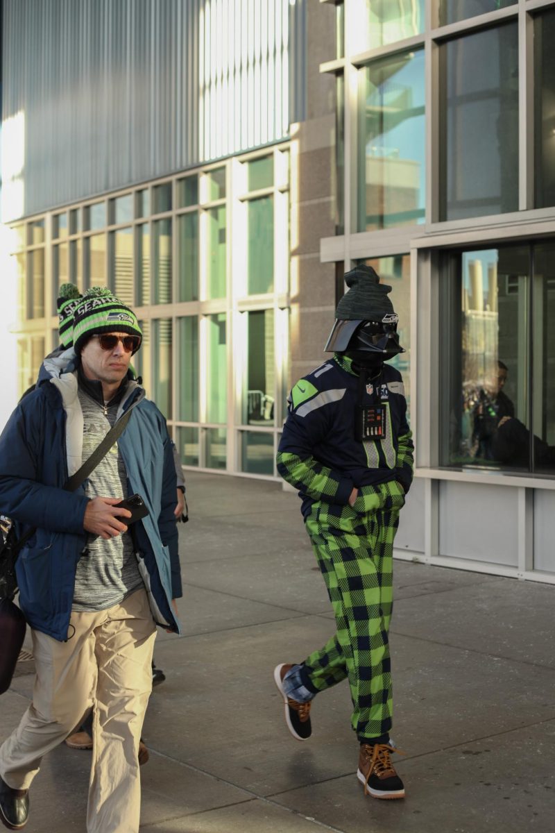 Three Seahawks fans adorned in team merch, and one who is also dressed in a Darth Vader costume.